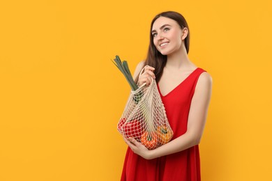Woman with string bag of fresh vegetables on orange background, space for text