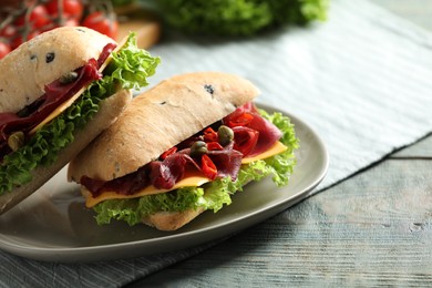 Photo of Delicious sandwiches with bresaola, cheese and lettuce on light blue wooden table, closeup. Space for text
