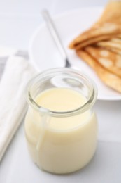 Photo of Tasty condensed milk in jar and crepes on white table