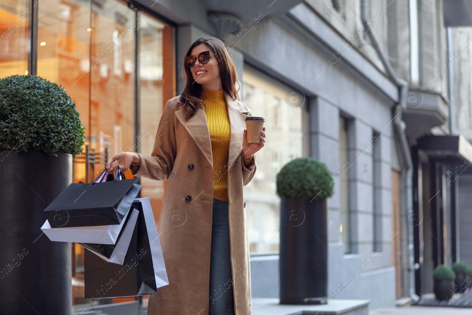 Photo of Beautiful young woman with cup of coffee and shopping bags on city street