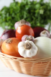 Photo of Fresh raw garlic and onions in wicker basket on table, closeup