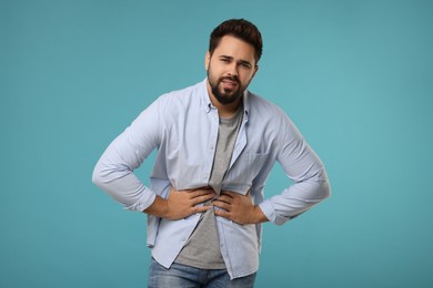 Photo of Young man suffering from stomach pain on light blue background