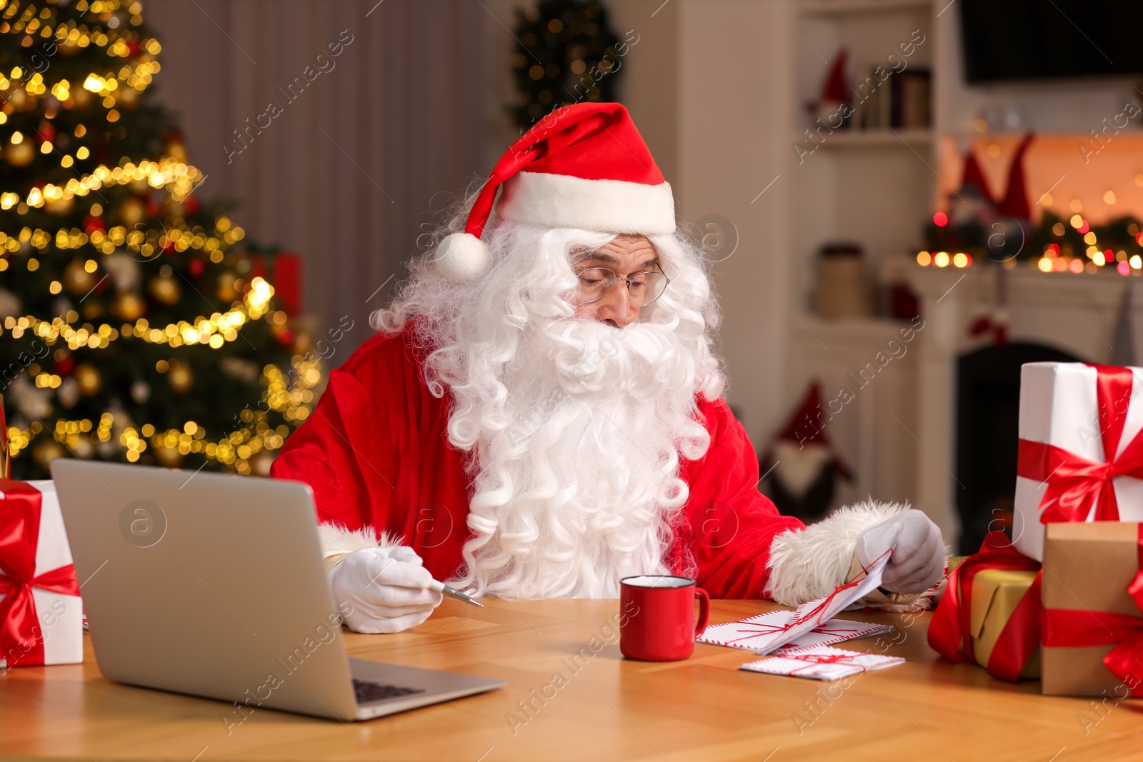 Photo of Santa Claus reading Christmas letters at table in room
