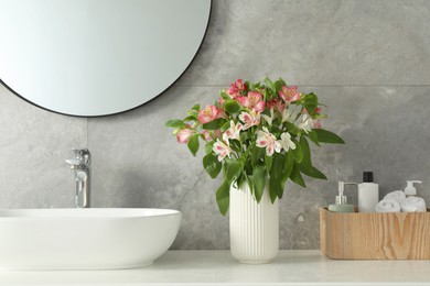 Photo of Vase with beautiful Alstroemeria flowers and toiletries near sink in bathroom