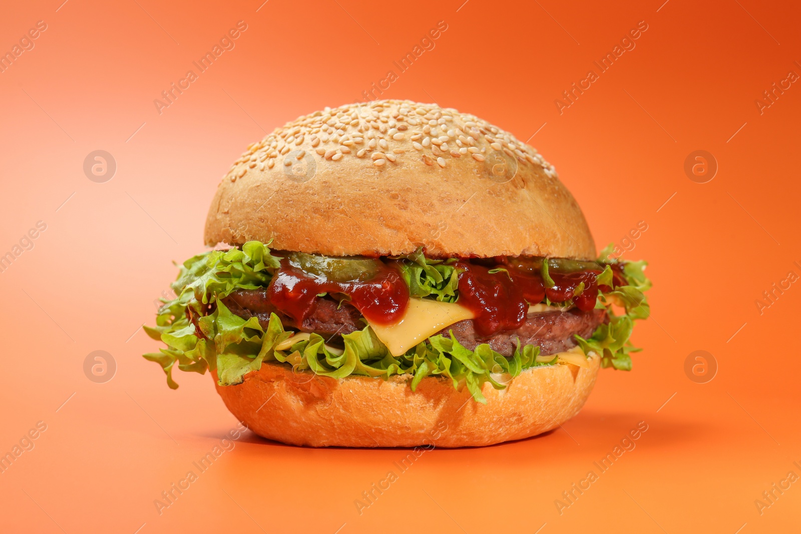 Photo of Delicious cheeseburger with lettuce, pickle, ketchup and patty on coral background, closeup