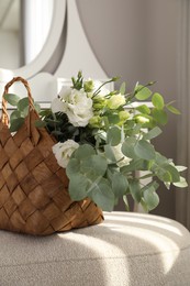 Stylish wicker basket with bouquet of flowers on ottoman in room