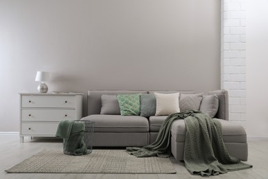 Large grey sofa and chest of drawers near light wall in room. Interior design