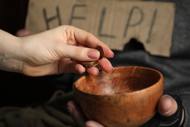 Photo of Woman giving coins to poor homeless man with bowl of donations and help sign, closeup