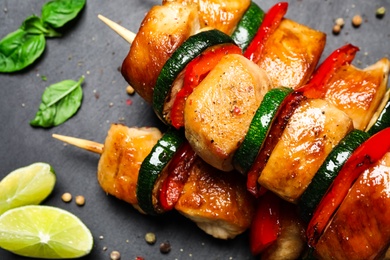 Delicious chicken shish kebabs with vegetables and lime on black table, flat lay