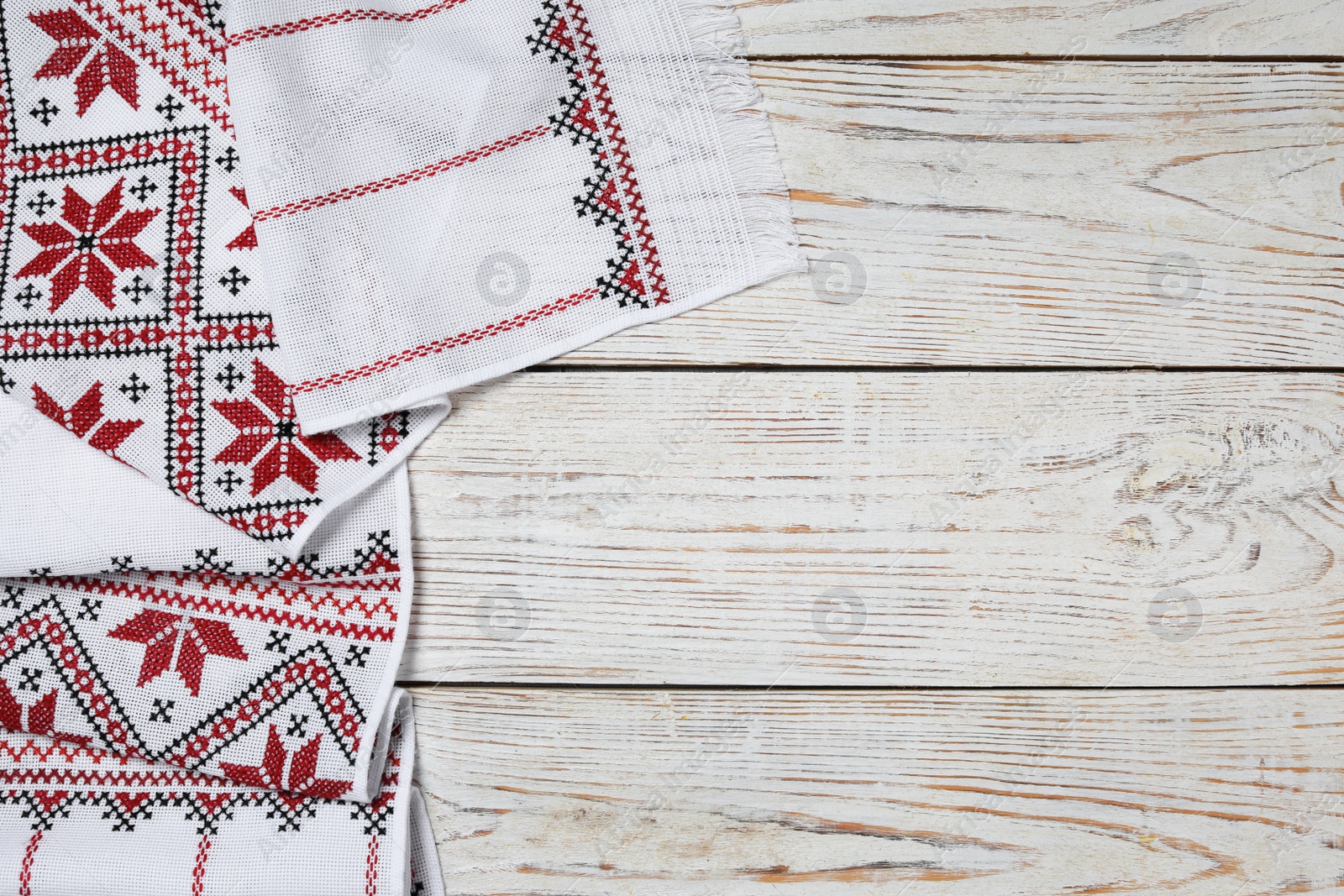 Photo of Beautiful rushnyk on white wooden table, top view with space for text. Ukrainian national embroidery