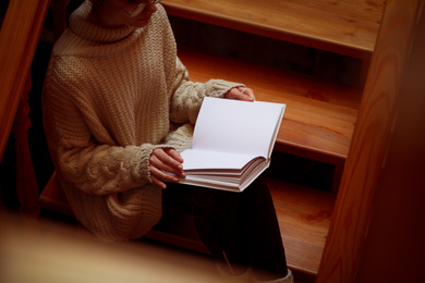 Photo of Woman reading book on wooden staircase, view from above