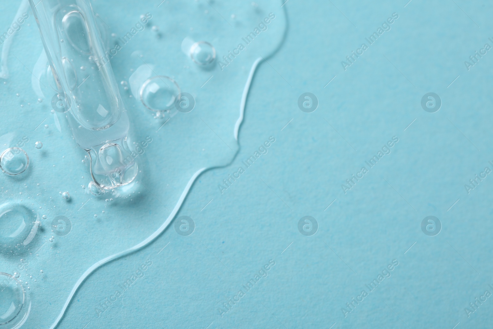 Photo of Dripping cosmetic serum from pipette onto light blue background, above view. Space for text