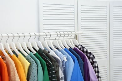 Photo of Rack with bright clothes in room. Rainbow colors