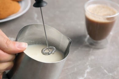 Photo of Woman using milk frother device in pitcher on table