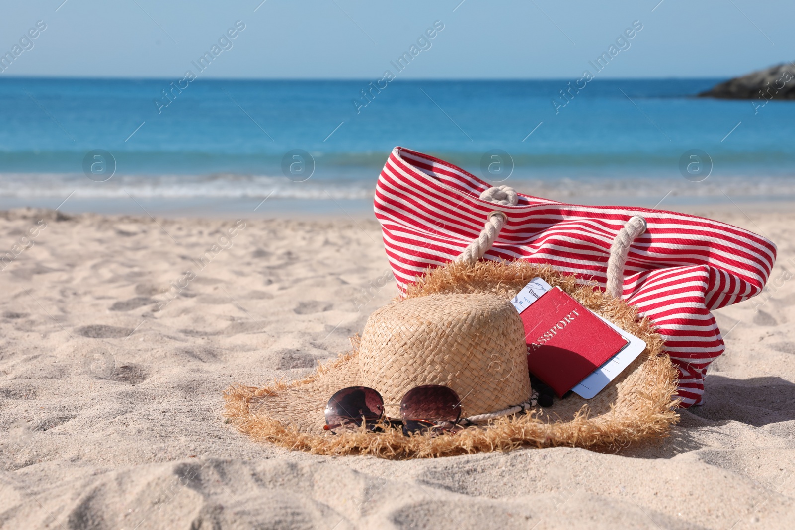 Photo of Straw hat with sunglasses, bag, passport and ticket on sandy beach