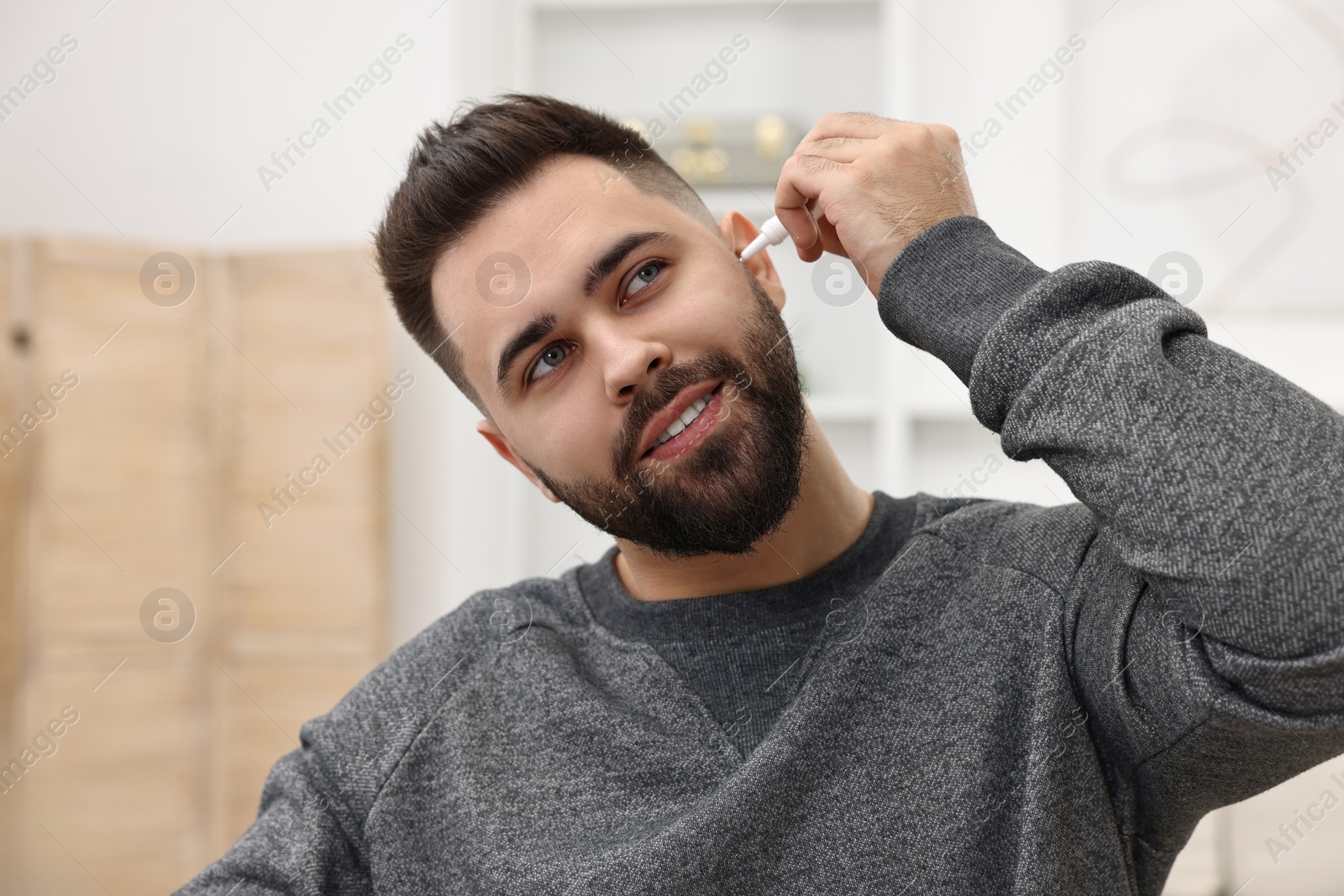 Photo of Young man applying medical ear drops indoors