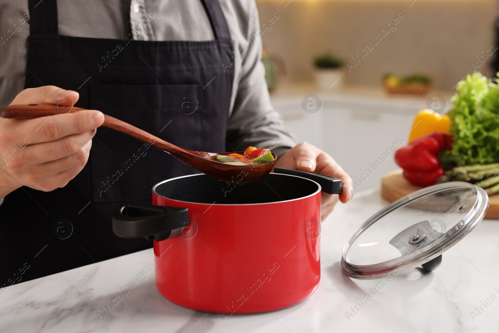 Photo of Cooking process. Man with pot of soup at white marble countertop in kitchen, closeup