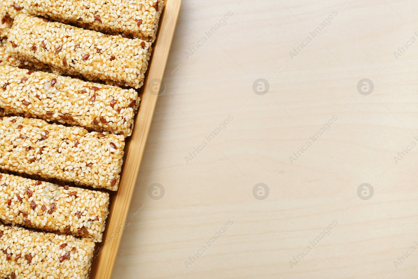 Photo of Plate with tasty sesame seed bars on wooden table, top view. Space for text