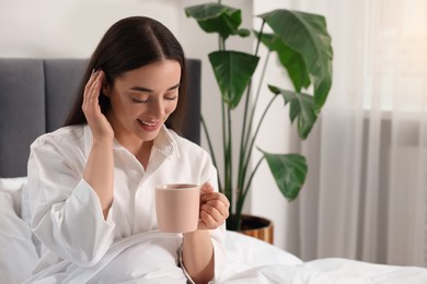 Happy woman with cup of drink in bed at home, space for text. Lazy morning