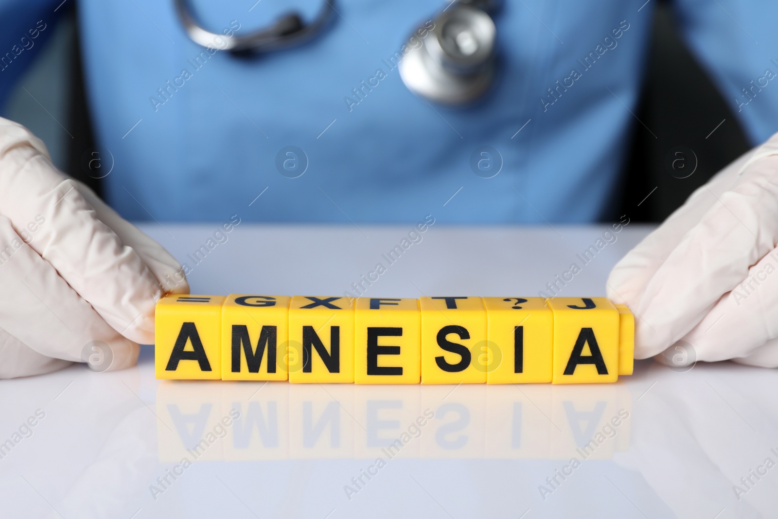 Photo of Doctor holding yellow cubes with word Amnesia at white table, closeup