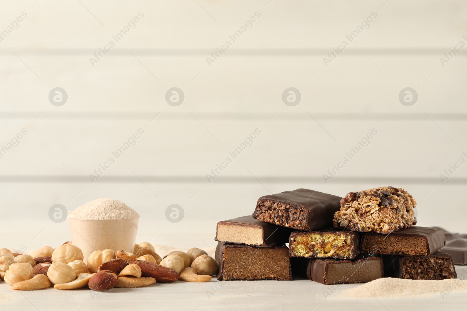 Photo of Different tasty energy bars, nuts and protein powder on white table, space for text