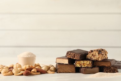 Different tasty energy bars, nuts and protein powder on white table, space for text