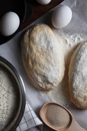 Photo of Raw dough, eggs and flour on parchment paper, flat lay. Cooking ciabatta