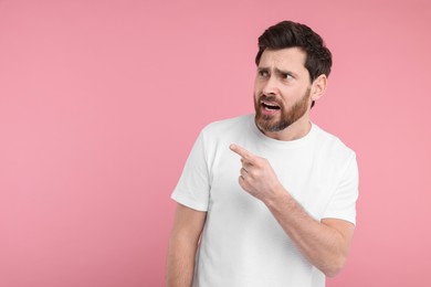 Photo of Surprised man pointing at something on pink background, space for text