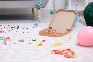 Photo of Pizza box with leftovers on messy apartment floor. After party chaos