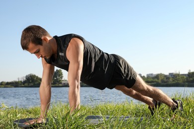 Photo of Sporty man doing straight arm plank exercise on green grass near river