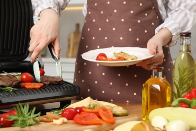 Photo of Woman cooking different products with electric grill at wooden table in kitchen, closeup