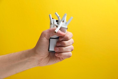Photo of Stop smoking. Man holding pack with broken cigarettes on yellow background, closeup