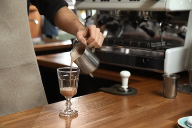 Photo of Barista pouring coffee into glass at bar counter, closeup. Space for text
