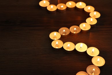 Burning candles on wooden table in darkness, space for text