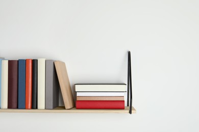 Photo of Wooden shelf with many hardcover books on white wall