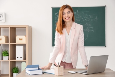 Beautiful young teacher standing near table in classroom