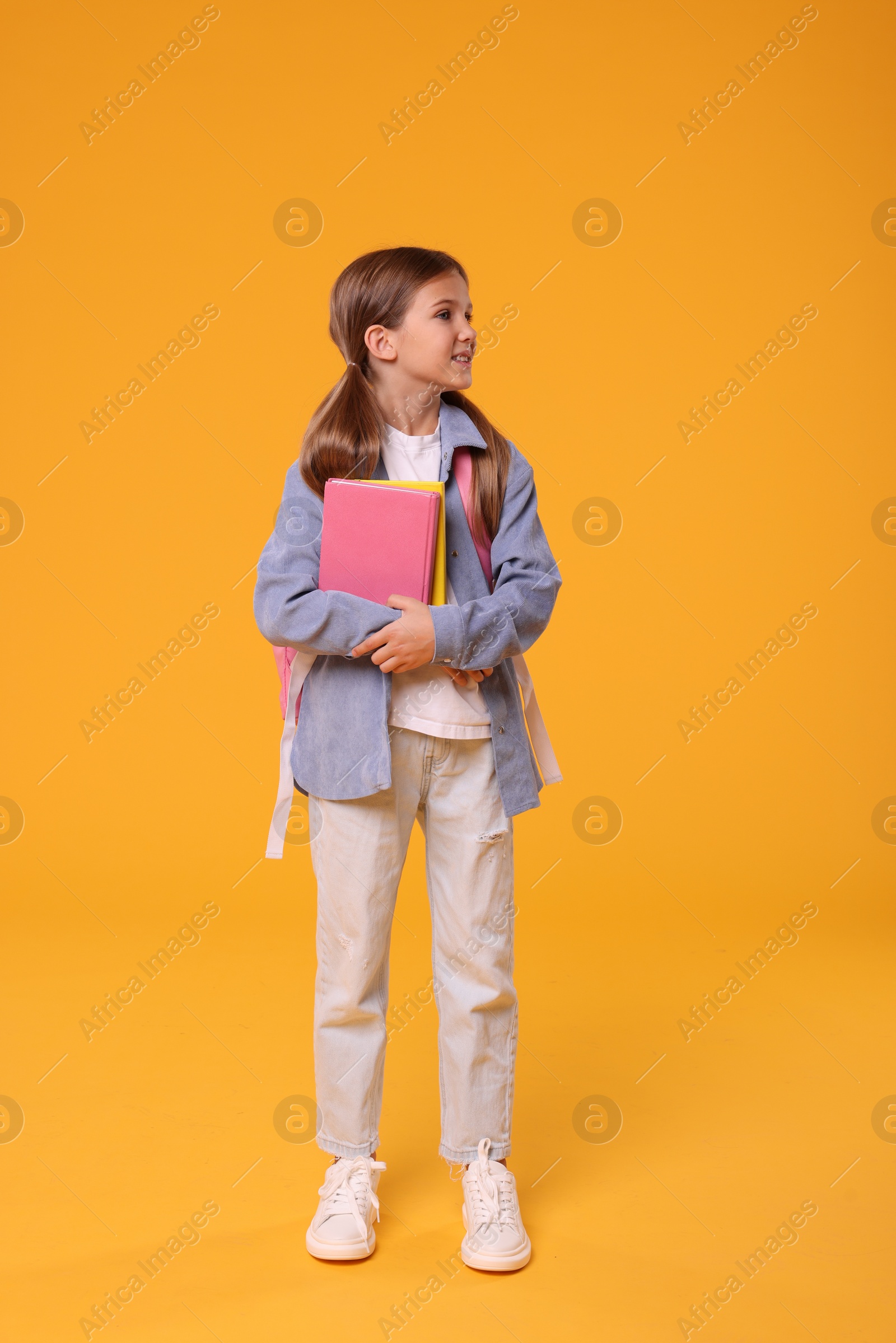 Photo of Happy schoolgirl with books on orange background