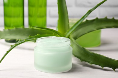 Jar of cosmetic gel and aloe vera leaves on white wooden table, closeup