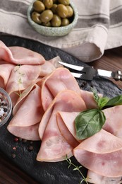 Photo of Tasty ham with basil, peppercorns and carving fork on table, closeup