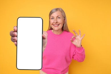 Image of Happy mature woman showing mobile phone with blank screen on golden background. Mockup for design