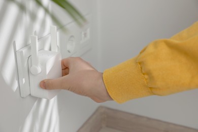 Photo of Woman turning on wireless Wi-Fi repeater indoors, closeup
