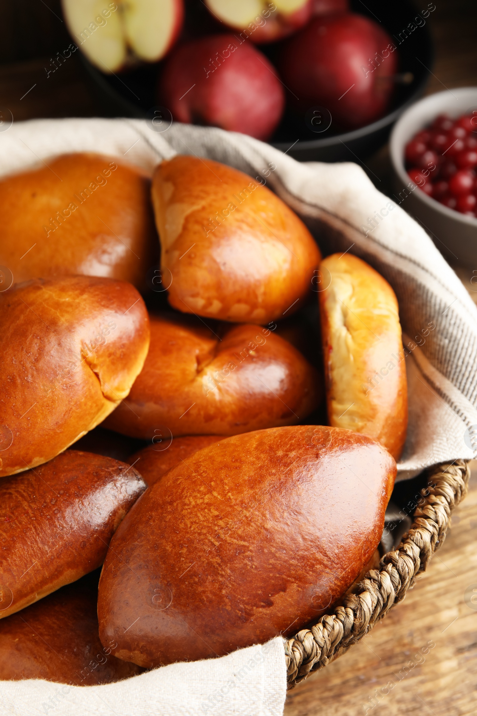 Photo of Delicious baked pirozhki in wicker basket on wooden table