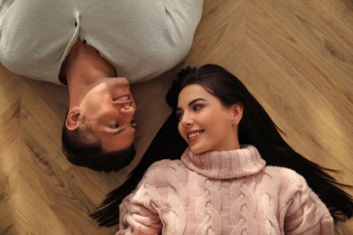 Photo of Happy couple lying on warm floor at home, top view. Heating system