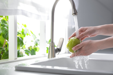 Woman washing apple over sink in kitchen, closeup. Space for text
