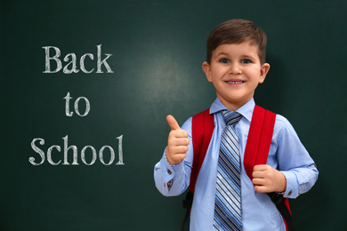 Image of Cute little child near chalkboard with phrase BACK TO SCHOOL