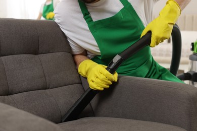 Photo of Professional janitor vacuuming armchair in room, closeup