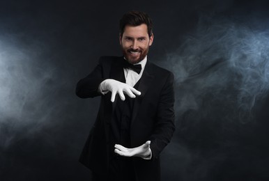 Happy magician holding something in smoke on dark background