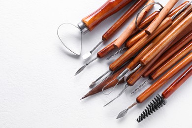 Photo of Set of different clay crafting tools on white textured table, flat lay. Space for text