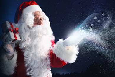 Santa Claus with gift blowing snow in winter forest. Christmas magic