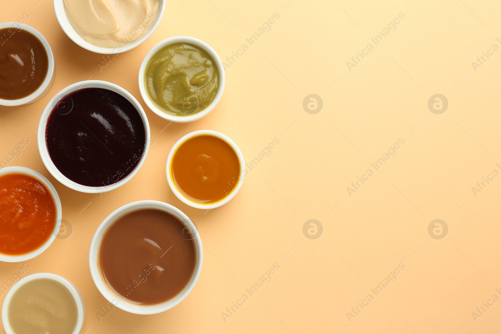 Photo of Bowls with healthy baby food on pale orange background, flat lay. Space for text
